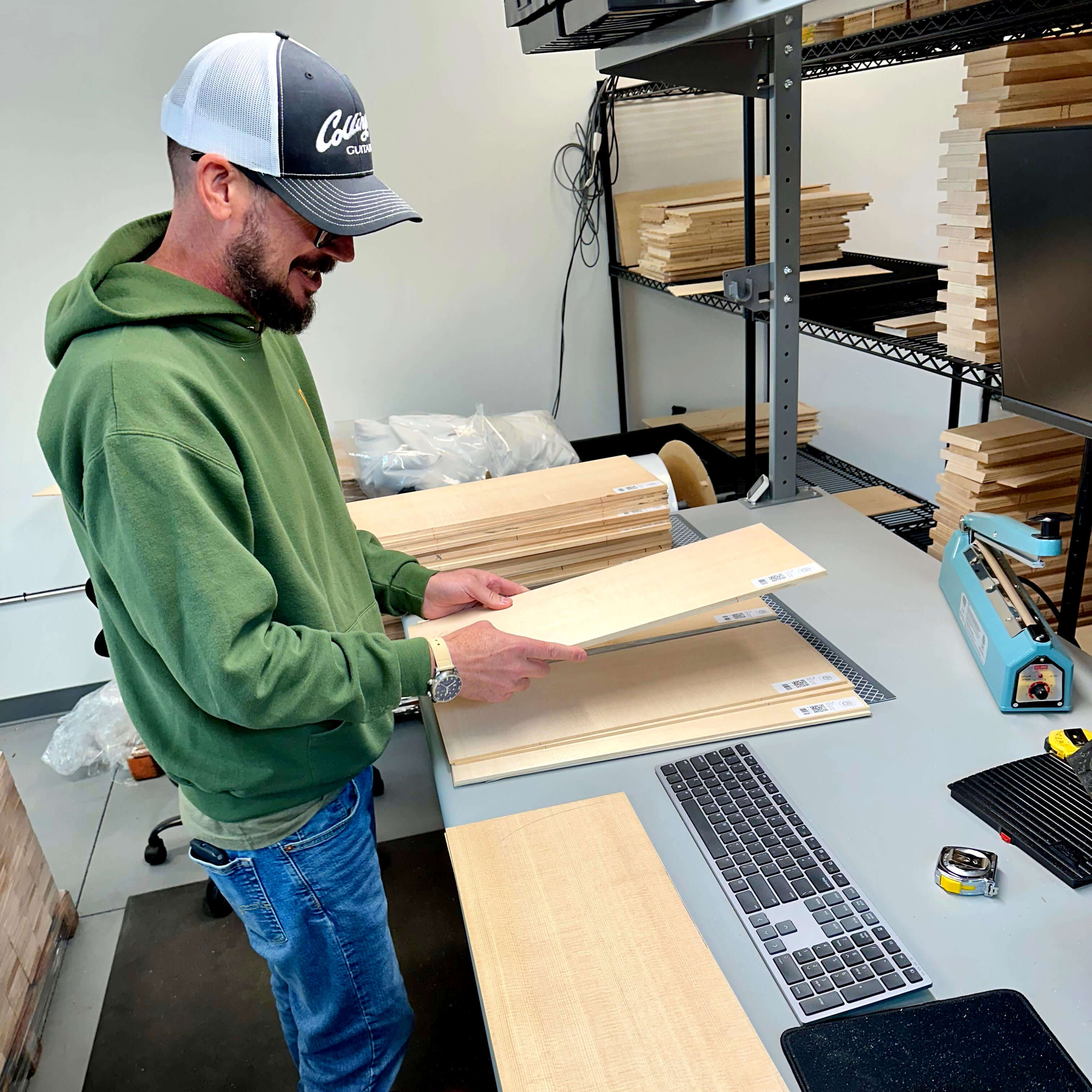 Man in green hoodie inspecting spruce soundboards at a grading station in a Pacific Rim Tonewood facility.