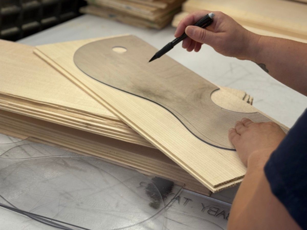 Luthier marking a softwood soundboard blank, outlining the guitar shape before cutting and voicing the top.