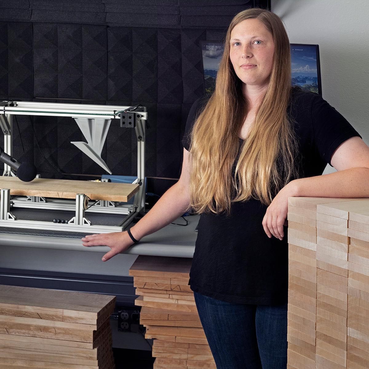 Alexis stands in a tonewood lab beside stacked billets, with acoustic testing equipment in the background.