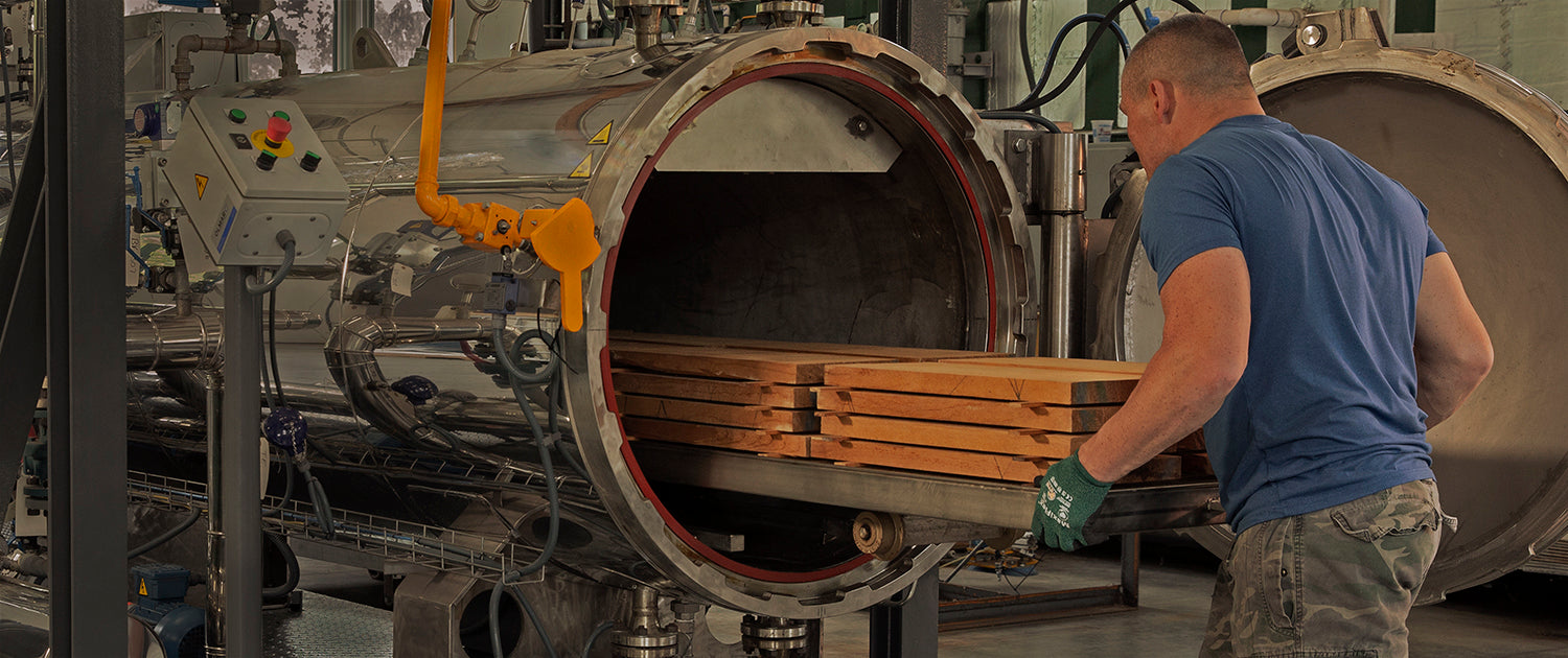 A worker in a blue shirt loads tonewood into a sizeable industrial autoclave. Machinery surrounds the area, conveying a busy, industrious atmosphere.