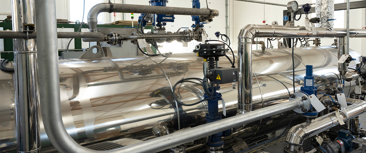 Industrial setting with polished metal pipes and valves, reflecting bright overhead lights. The scene conveys a clean, efficient atmosphere.