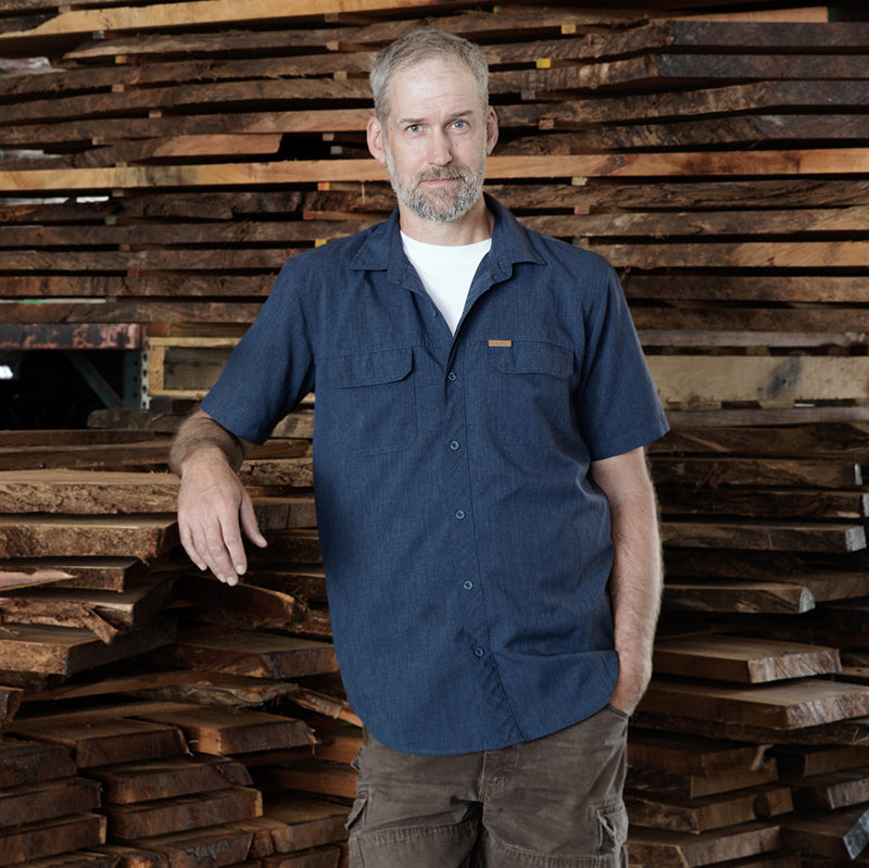  A man stands before a pile of tonewood, posing for a picture.

