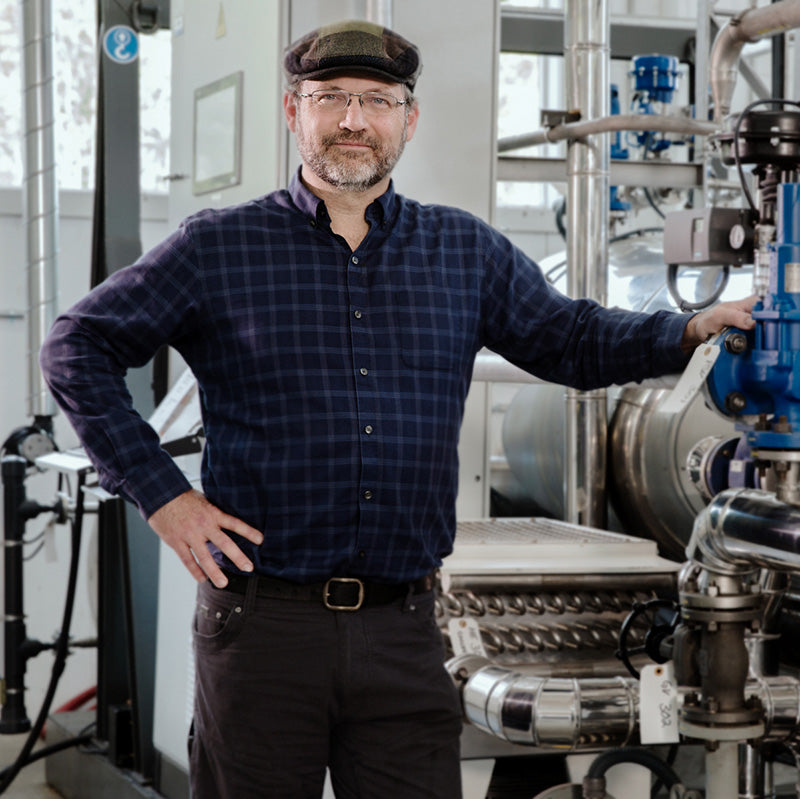 A man wearing a hat stands next to a machine, visible in the background.