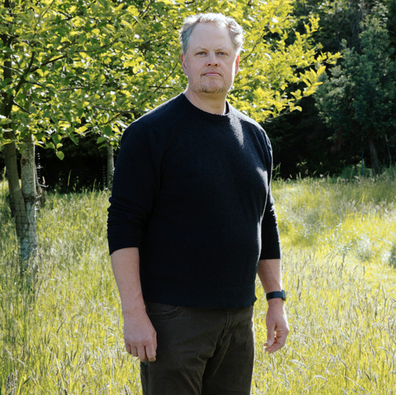 Eric Warner is standing in a field with a tree visible in the background.