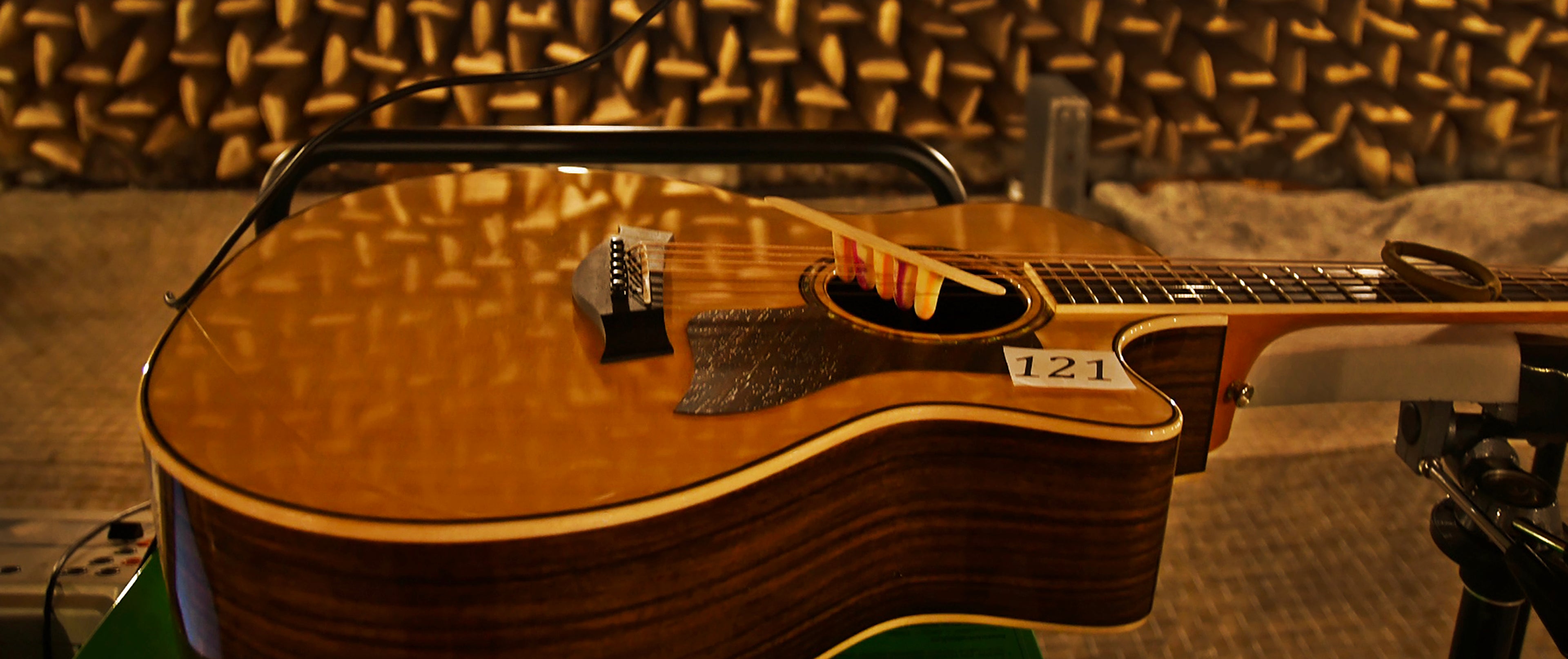 Acoustic guitar with a glossy finish placed under a microphone, set against a soundproof room with foam spikes, creating a serene, studio ambiance.