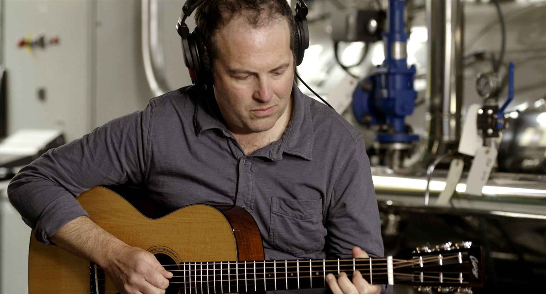 Jacob Navarro is playing an acoustic guitar while wearing headphones.