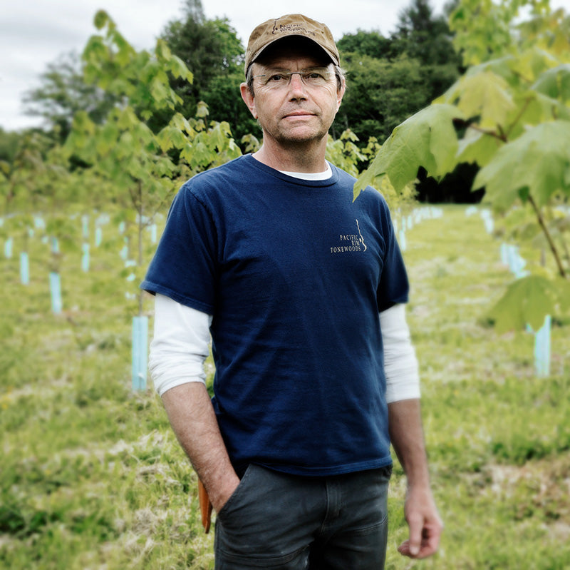 Kevin Bruke is standing in a forest of trees, enjoying the nature around him.
