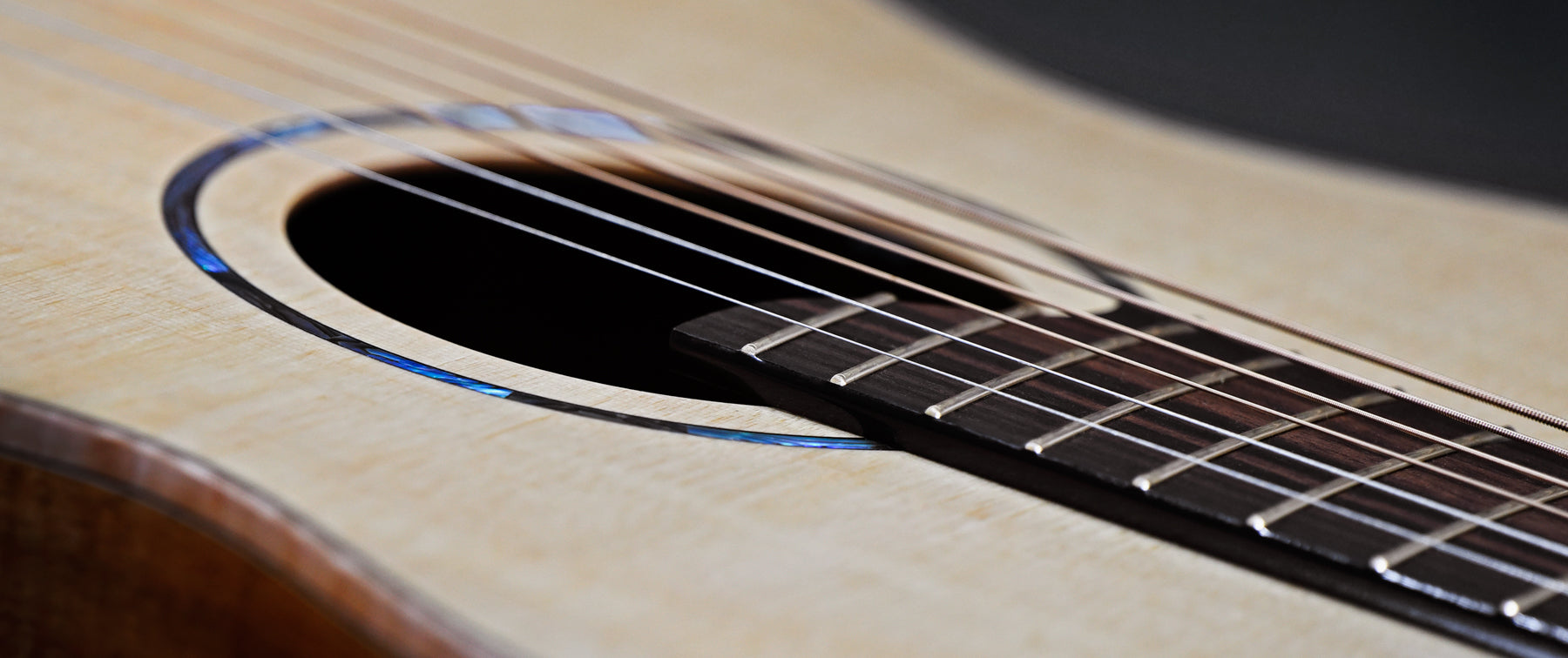 This is a close-up of a Sonically Graded acoustic guitar's strings and soundhole. The wooden body has a smooth finish and detailed inlay around the soundhole, creating a serene mood.