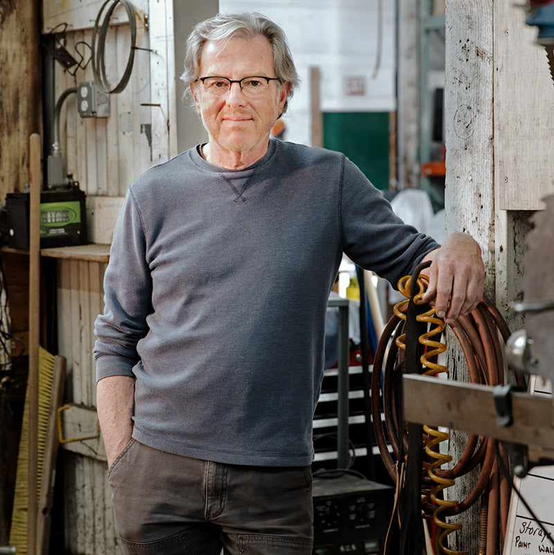 A man in blue clothing stands next to a variety of tools.
