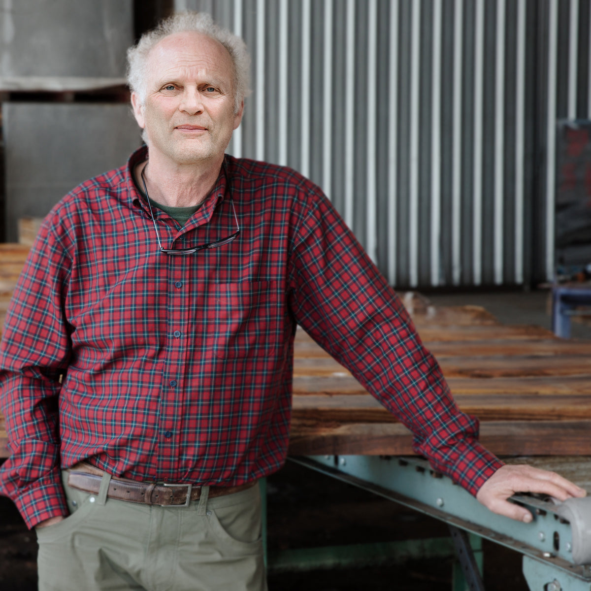 Steve McMinn stands in front of neatly stacked tonewood at Pacific Rim Tonewoods. He wears a red plaid shirt and looks directly at the camera.