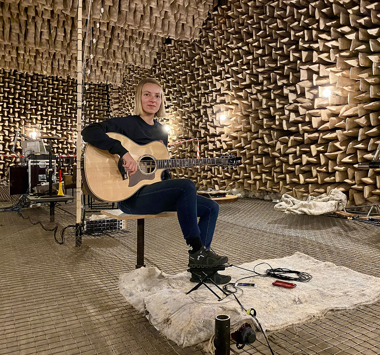 Musician seated in an anechoic chamber playing an acoustic guitar during tonewood testing.