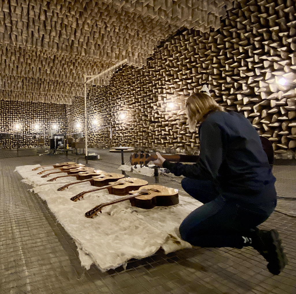 A person testing a row of guitars in an anechoic chamber lined with acoustic foam wedges.